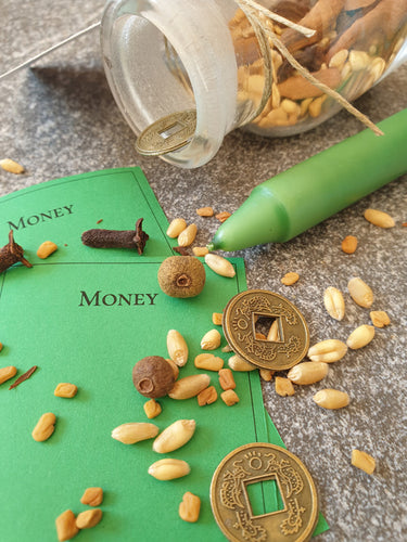 Money Witch bottle containing Wheat, Cinnamon, Allspice, Clove, Fenugreek Seeds lying next to Green Candle, 2 green scrolls, coins and spilt contents