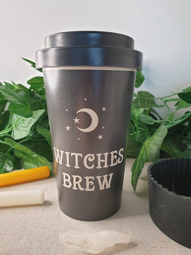 Black Witches Brew Bamboo Travel Mug with rubber sleeve near candles